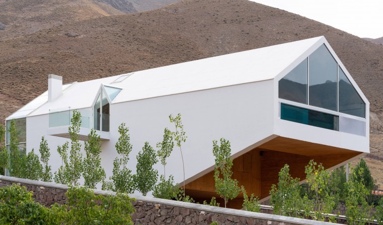 Side view of the gabled white form with cantilevered patio cover seen from above the stone retaining wall