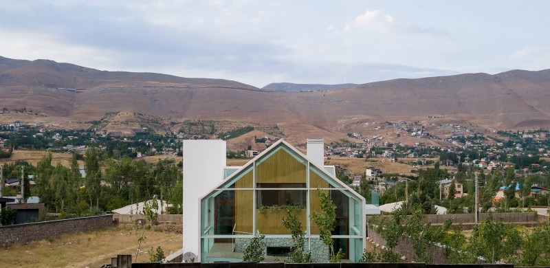 Front facade with the white form framing the gabled green-glass volume and the mountain backdrop