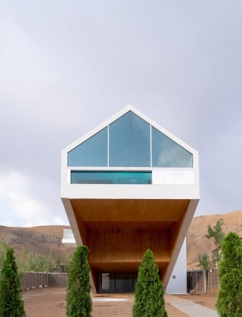 Front view through cypress trees of the gabled glass volume above the cantilever