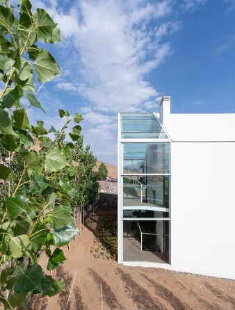 Side view of the vertical glass greenhouse rising next to the gabled white volume