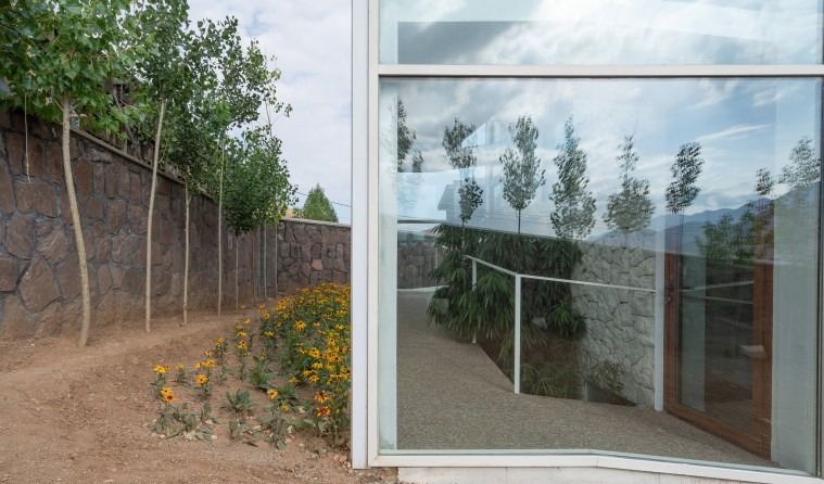 Side stone retaining wall with greenhouse glass and yellow marigolds in the foreground