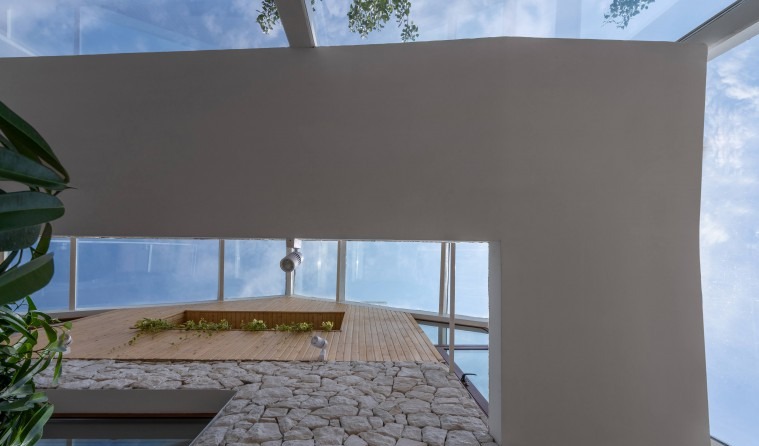 View up from the stone-clad corridor toward the wood-deck floor and glass roof above