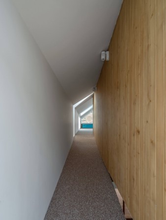 Sloped attic corridor with white sloped ceiling and wood-clad wall ending at the triangular pool window