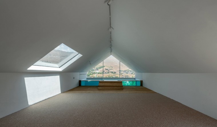 Empty attic room with skylight on one side and triangular window opening to a view of the village and mountains