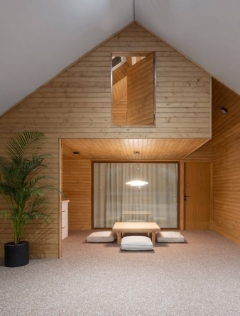 Bedroom interior with low Japanese-style table, floor cushions and triangular skylight in the wood-clad ceiling