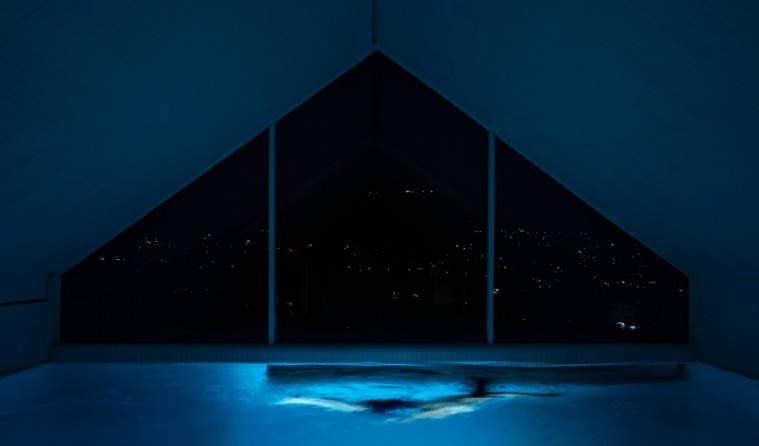 Indoor pool with the night city view through the triangular window and a swimmer in the lane