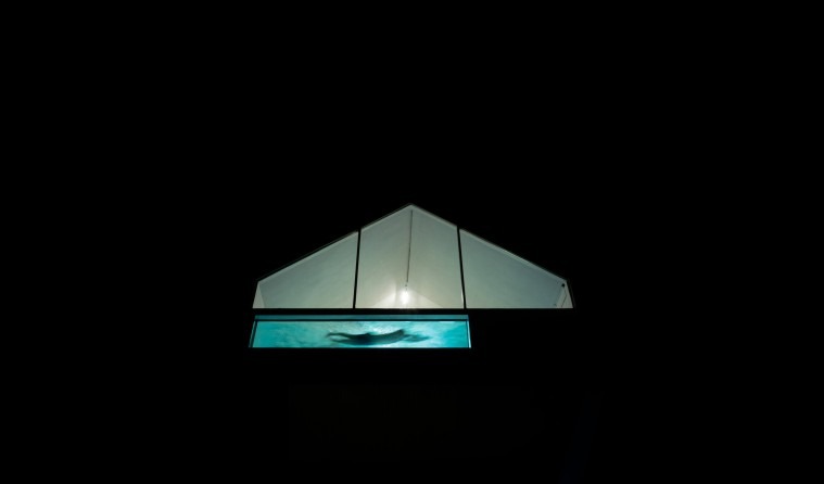 Glowing skylight pool at night seen from outside, suspended above the dark patio