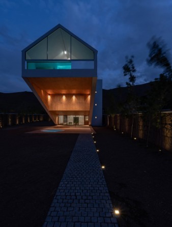Twilight front exterior with entrance path lit by ground-level lights leading to the glowing under-cantilever