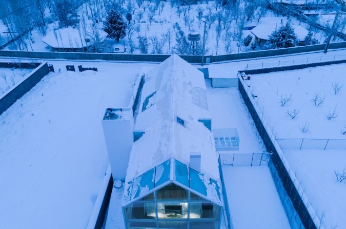 Top-down aerial in snow showing the ridge of the roof with skylight and a small visible pool inside the gable