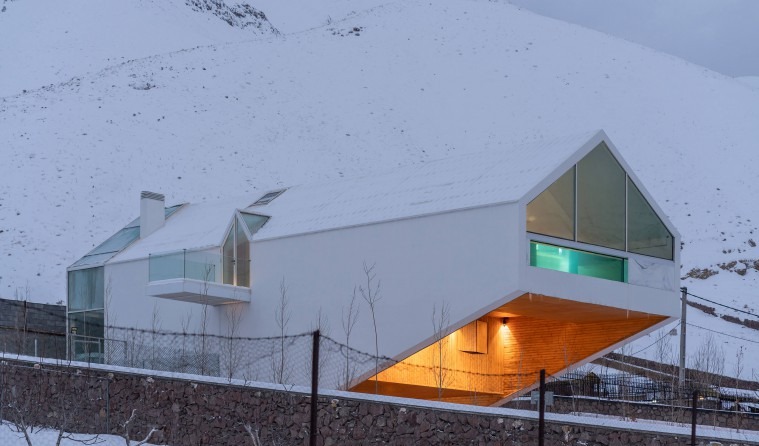 Snow exterior with the snow-covered mountain backdrop and the warmly lit interior under the cantilever