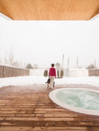 Snow patio with woman in red sweater and small dog walking toward the jacuzzi