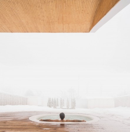 Jacuzzi in winter fog with figure submerged and snowy landscape beyond