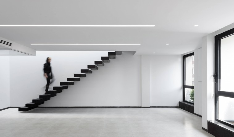 Open office floor of Kar-Khaneh with the cantilevered black stair zig-zagging across the white wall