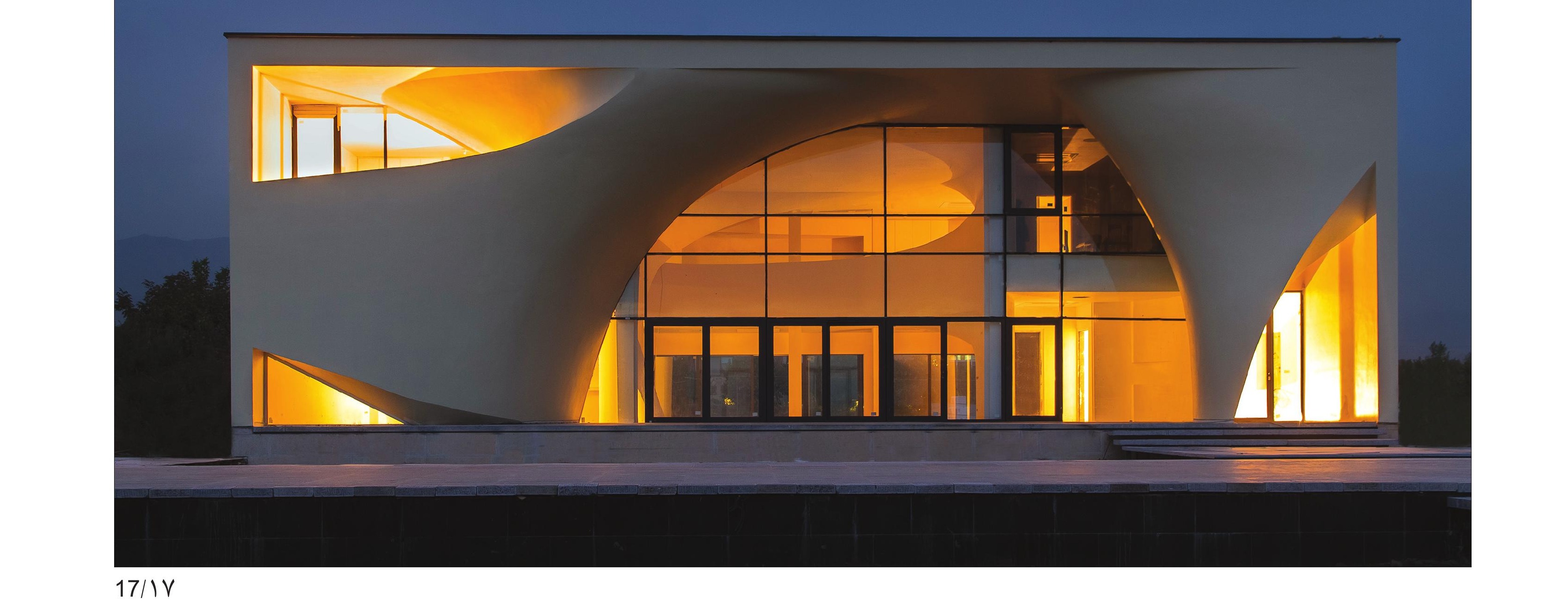 Glowing night facade with curved cantilever and tall arched glass opening