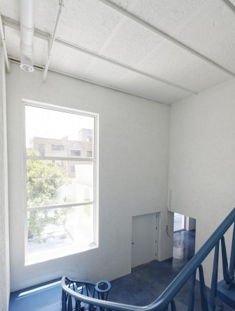 Light-filled upper landing of Nabshi Gallery — a tall window, white walls and the deep blue resin floor curling up the wall