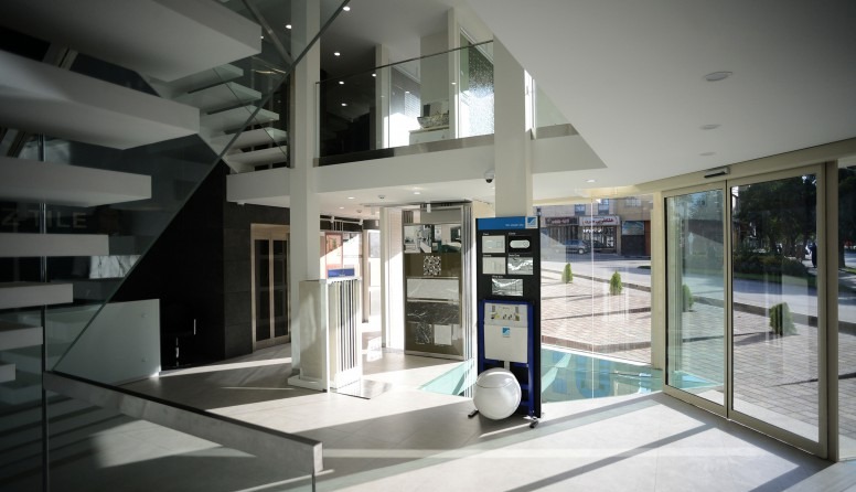 Night view of the tile showroom entrance: the lower travertine plinth and white showroom volumes glow against the dark sky