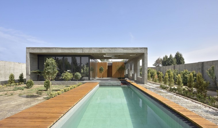 Daytime hero view from the south: the deep concrete frame projects over the pool, the long timber deck lining the water,
