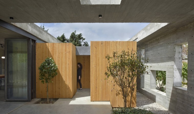 Two wood-clad private volumes facing one another across the court: a figure slips between them, the seam between boxes b