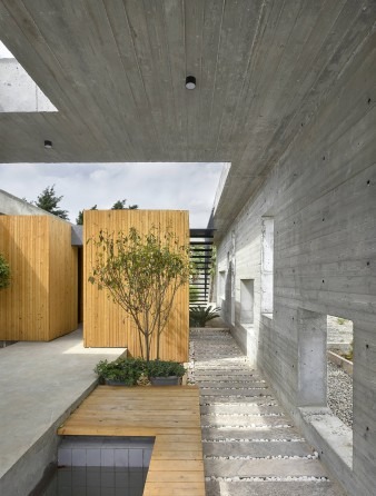 Looking past the wood-clad volume toward the long perforated concrete wall: the gap of stone gravel between deck and wal