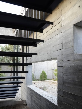 The floating black steel stair against the rough board-formed wall: the only vertical move in the project, leading from 