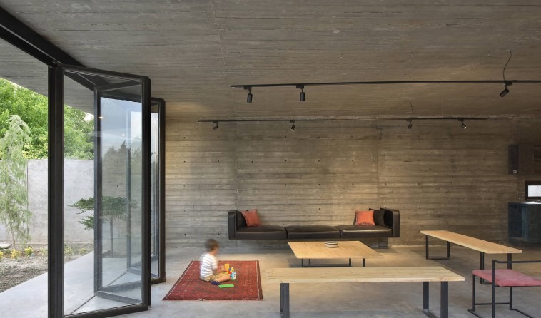 A child plays on a red Persian rug in front of the concrete wall: the project's heavy materials soften under the everyda