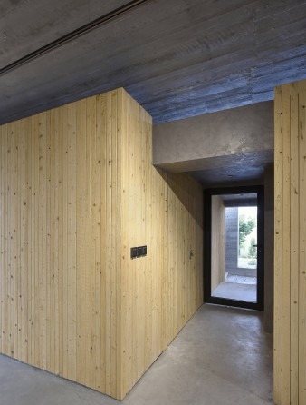The narrow entry corridor between two wood-clad volumes: the project's threshold is not a door but a slot of wood within