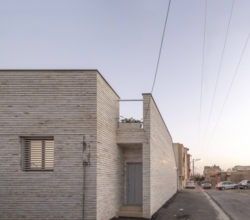 Side alley view of the stone-clad facade with the parapet of the roof courtyard visible at the upper level