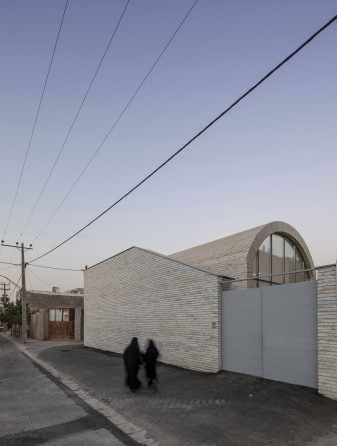 Twilight street view with two veiled figures walking past the entrance, showing the corner of the white house and the vault rising above the side wall