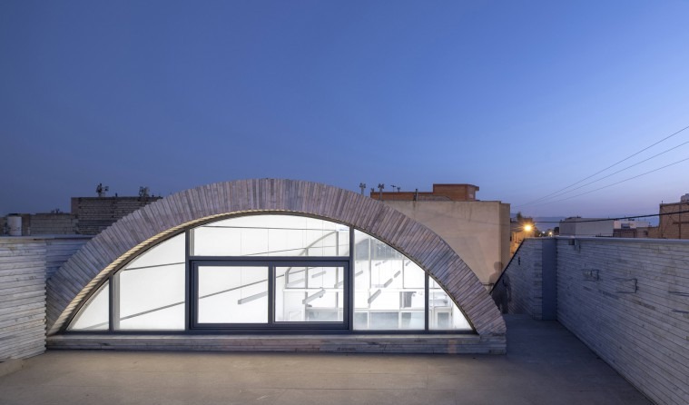 Rooftop view at dusk showing the back face of the vault opening as a glazed wall onto the small roof courtyard