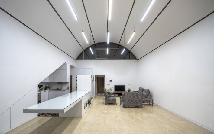 Wide-angle interior view showing the entire single vaulted space — kitchen counter, living seating, dining and the rear skylight under the curve